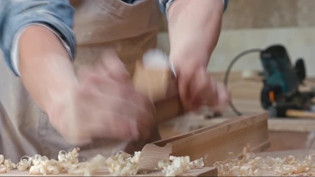 Mid-section of male carpenter shaping wood plank with hand plane, then checking his work