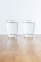 2 full glasses of clear healthy water standing on a wooden table