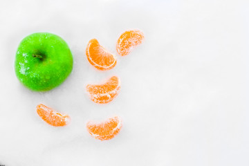 Green apple and slices of tangerines in the snow. Beautiful winter composition.