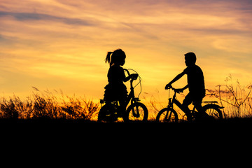 Fototapeta na wymiar silhouette little boy and little girl having fun riding bike on sunset 