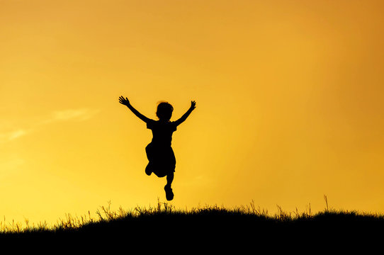 silhouette happy little girl jumping to sky on sunset
