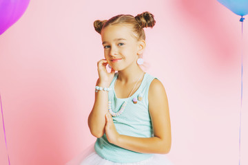Little girl with bright accessories and a candy on a pink background