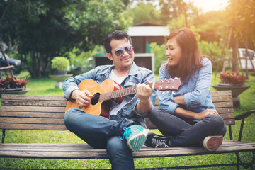 Young couple in love playing acoustic guitar in the park while s
