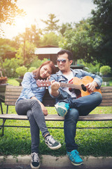 Young couple in love playing acoustic guitar in the park while s