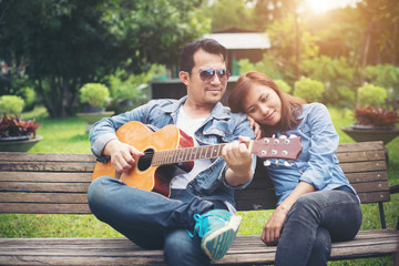 Young couple in love playing acoustic guitar in the park while s
