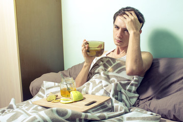 young man lies in bed sick with colds and flu