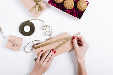 Female hands with red manicure pack the gifts in boxes and tie t