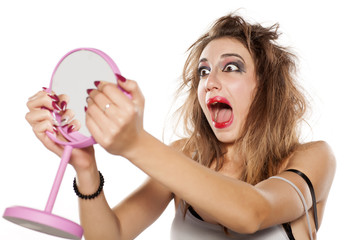 shocked young woman with bad makeup and messy hair looking at herself in the mirror