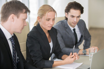 Group of three business partners discussing new project at meeting in office room, using laptop. Middle aged businesswoman explaining ideas, looking presentation on screen. Business success concept