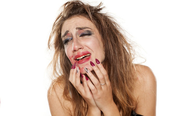 crying young woman with messy hair smudge her makeup with hand