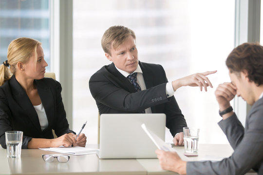 Furious boss scolding young frustrated intern, dismissing him with hand gesture. Ineffective stressed office worker receiving dismiss notification sitting at table, listen to irritated boss yelling