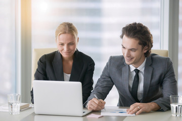 Group of two business partners discussing new project at meeting in office room, using laptop. Middle aged businesswoman and her young colleague browsing presentation on screen. Business concept