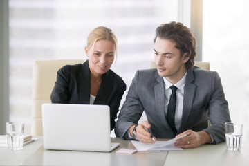 Group of two business partners discussing new project at meeting in office room, using laptop. Mid aged businesswoman and her young associate browsing presentation on screen. Business concept