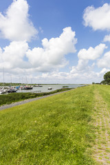 Grass dike in Friesland with blue sky with white clouds