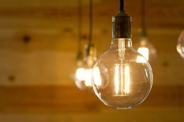 Closeup image of a turned on light bulb over a wooden background. - Powered by Adobe