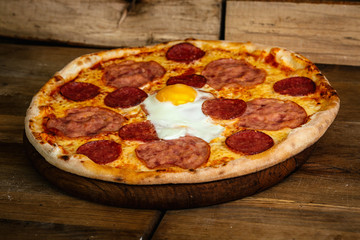 Pizza with sausages and egg on wood background