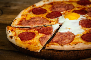 Pizza with sausages and egg on wood background