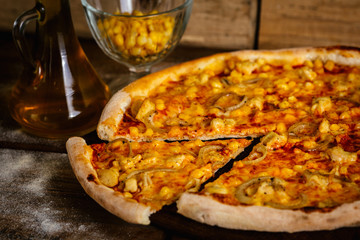 Whole pizza with chicken and corn on wood table with ingredients