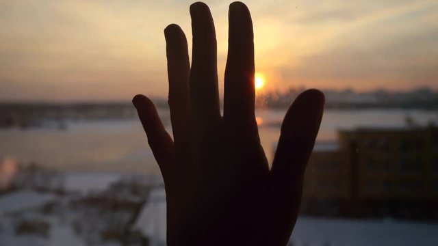 Women hand touches the sun by the window on sunset city background. 3840x2160