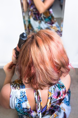 Fototapeta premium Closeup portrait of young woman using curling iron on hair looking into mirror