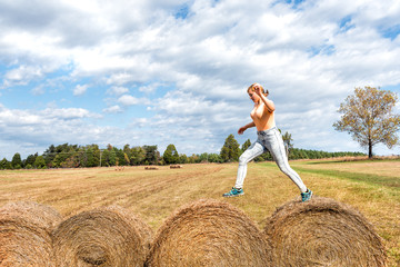 Naklejka na ściany i meble Young woman jumping over hay roll bales in a field