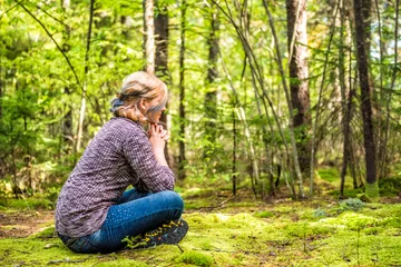 Fotobehang Young woman sitting on mossy ground in forest thinking © Andriy Blokhin