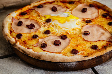 Pizza with ham, sausages and egg on wood background