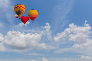 Hot air balloon rises very high in blue sky above white clouds