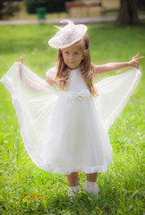 Little girl on the lawn in a white dress and a hat