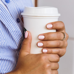 Woman in a blue shirt and pink manicure holding a white cup with two hands close up