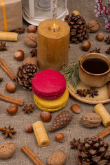 Fototapeta na wymiar Cup of coffee, macaroons, cookies, walnuts, hazelnuts, cinnamon sticks, star anise, cone, candle, fir branch on sackcloth fabric