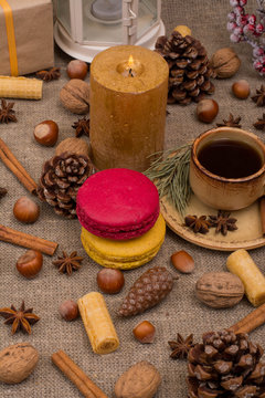 Cup of coffee, macaroons, cookies, walnuts, hazelnuts, cinnamon sticks, star anise, cone, candle, fir branch on sackcloth fabric