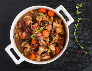 Beef Bourguignon in a casserole on black stone. Stewed with bacon, garlic, carrots, onions, mushrooms,  red wine, fresh thyme and spices. Top view.