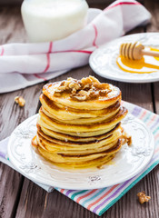 Homemade pancakes with honey and walnuts, vintage white plate, dipper, milk in glass jar, dark wooden table.