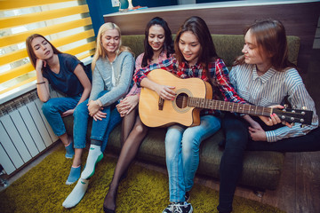 Obraz premium Beautiful girls sitting on couch, have fun and play the guitar in Hostel.