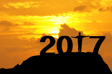 Silhouette of a man open hands on top of mountain during sunset to complete 2017 year.
