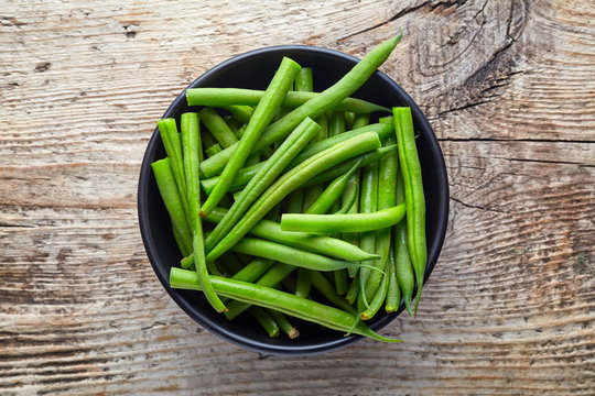 Bowl of green beans on wooden table, from above