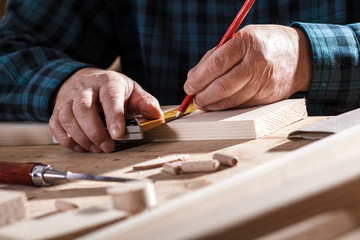 Fototapeta na wymiar Close up of senior carpenter hands taking measurement on a wooden plank in workshop