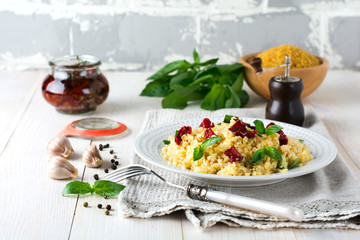 Bulgur with dried tomatoes and basil on a light wooden background. Vegetarian dish. Selective focus.