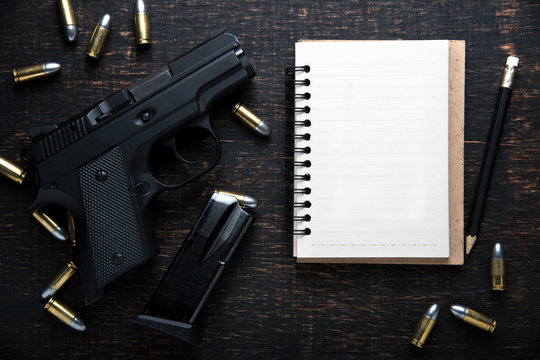 Gun and ammunition and blank notebook on dark wooden table. top view
