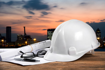 safety helmet and architect plant on wood table with city sunset scene and building construction