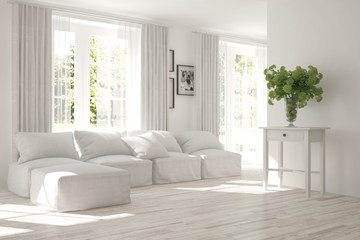 Fototapeta premium White room with sofa and green landscape in window. Scandinavian interior design