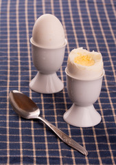 Egg cups with an eggs on top of a dark blue table cloth, with a spoon