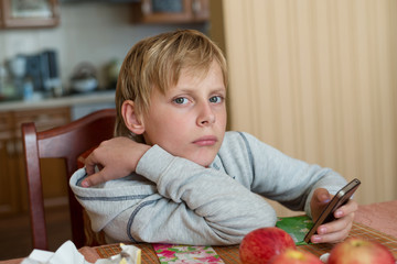 Naklejka premium Boy sitting at table at home with the phone