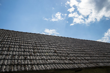 Close up of aged roofing tiles on old house in village. A lot of moss on tiled roof of hovel. Countryside scene