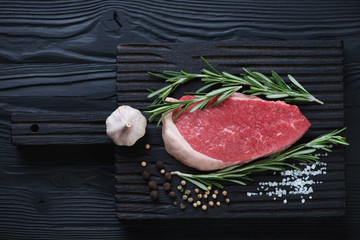 Black wooden chopping board with raw seasoned beef medallion