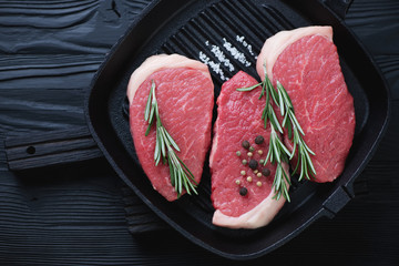 Cast-iron grill pan with raw beef medallion steaks, top view