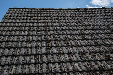 Close up of aged roofing tiles on old house in village. A lot of moss on tiled roof of hovel. Countryside scene