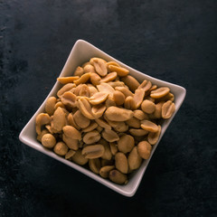 Top view on white bowl full of salted peanuts
