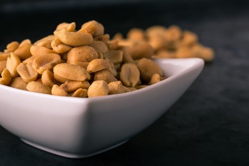 White square bowl full of salted peanuts
